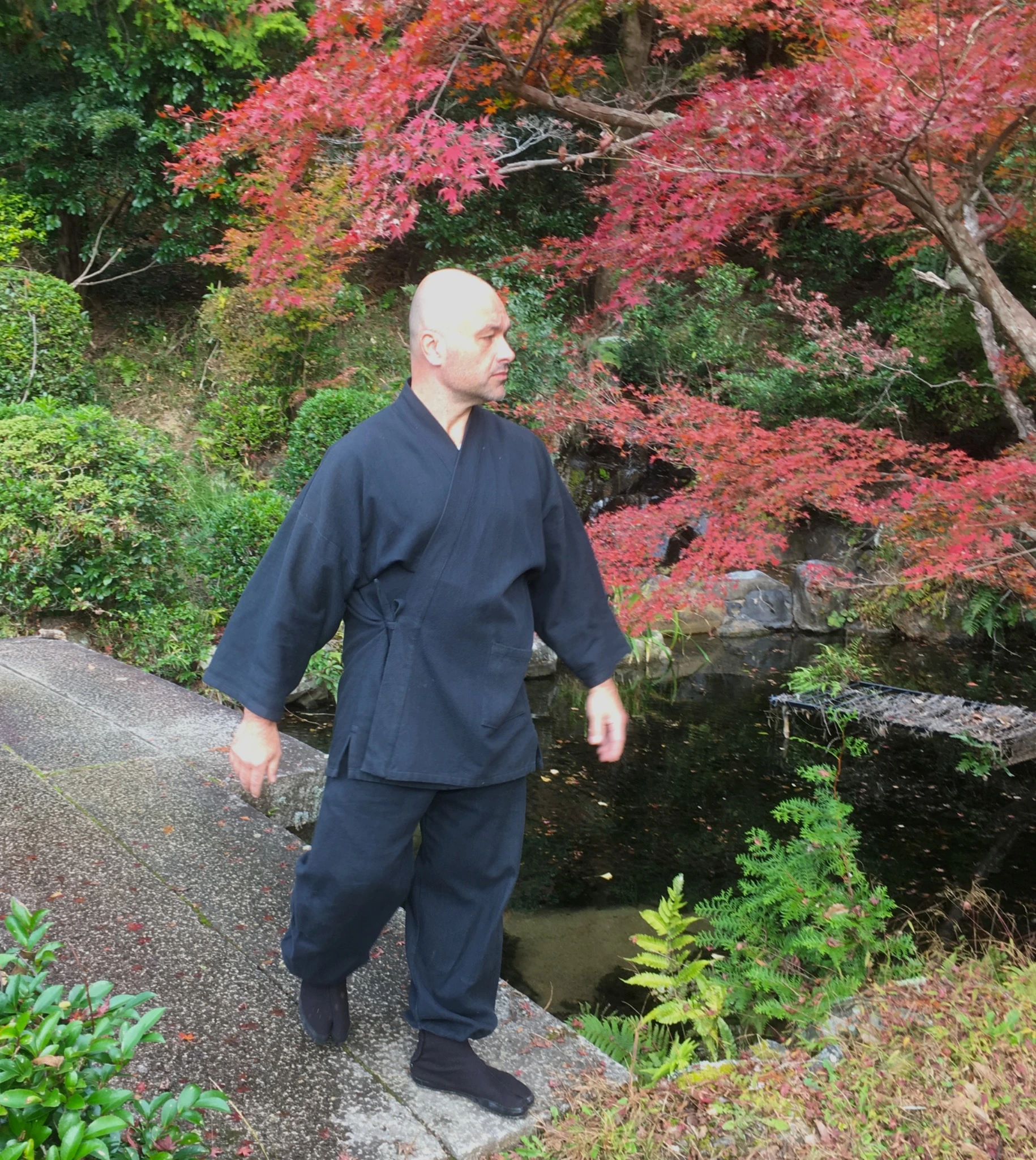 赤く色づいた木々に囲まれた小道に立つ、黒い刺し子の作務衣姿のジェローム・パイエット。