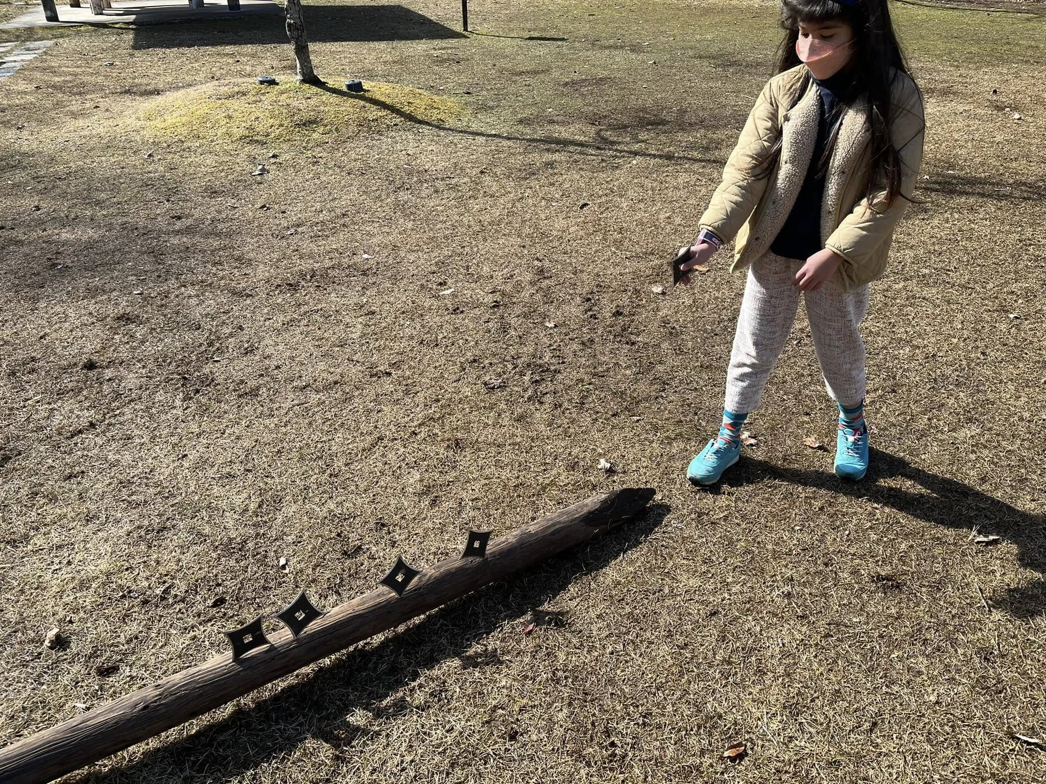 屋外で、千盤手裏剣が刺さった木製標的の前で稽古するジェローム・パイエットの娘。